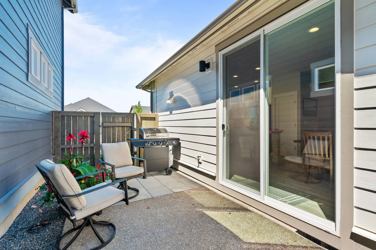 A welcoming outdoor patio area featuring a built-in grill, comfortable seating, and vibrant flowers providing a cheerful backdrop. The space is set up for casual dining and social gatherings under the open sky.