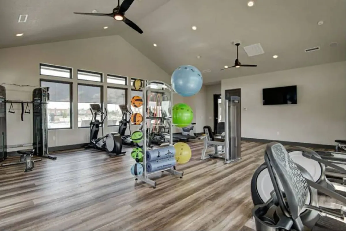 A bright, modern gym equipped with various exercise machines, colorful exercise balls, and large windows letting in natural light. The space feels motivating and is designed for both individual and group fitness activities.