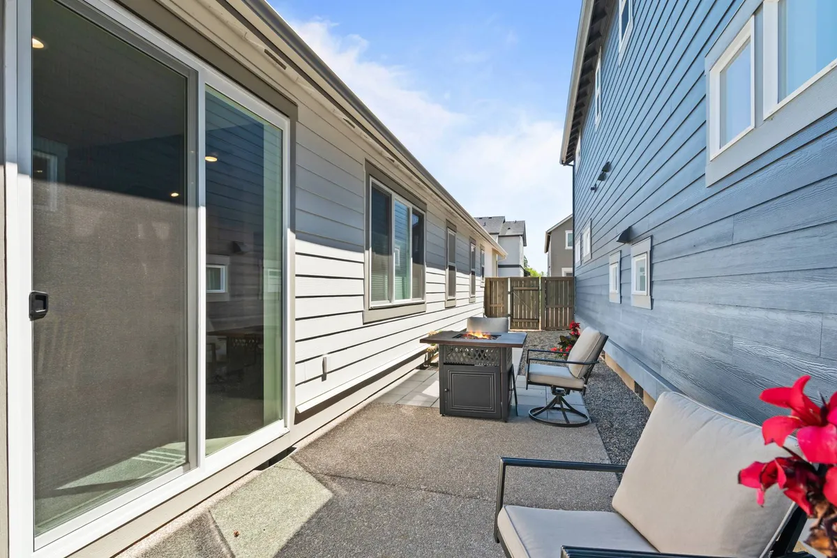A tranquil exterior patio scene with comfortable seating, a table adorned with decorative elements, and a sliding glass door leading inside. The setting invites relaxation with views of the outdoors, ideal for private moments or small gatherings.