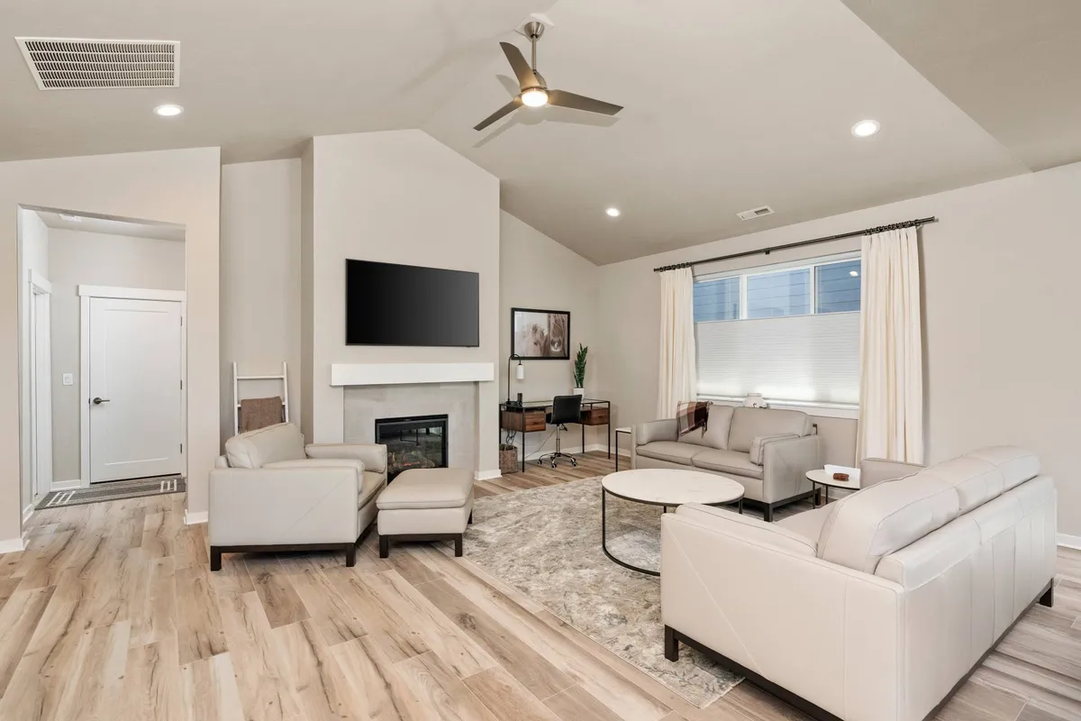 This image features a comfortable living room with a sofa set, coffee table, fireplace, TV, and a desk with a chair. The space is designed for relaxing, entertaining, and spending time together, with plenty of seating and a cozy atmosphere.