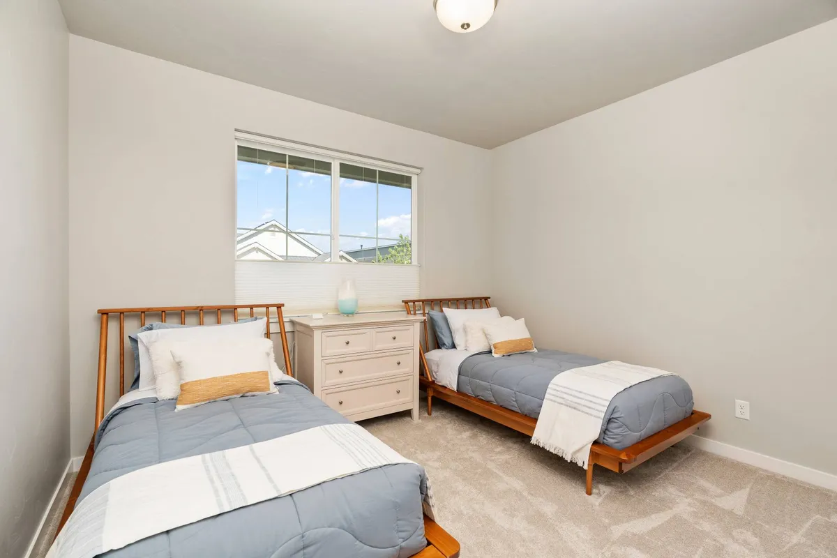 A calm, welcoming bedroom with two twin beds, a dresser, and a window letting in natural light. The room is arranged for flexibility, offering comfort for families or groups while maintaining a peaceful ambiance.