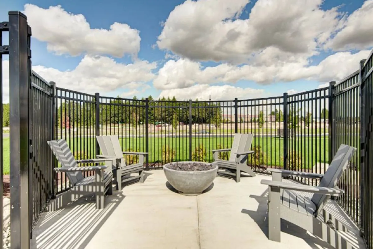 This exterior image features a cozy fire pit surrounded by comfortable seating, a well-maintained grassy area, and privacy fencing. The scene is set under a cloudy sky, giving it a tranquil yet inviting ambiance for unwinding or informal gatherings.